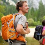 The boy is ready for hiking, wearing an orange branded backpack.