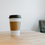 A coffee sleeve in white color with black cap can customized by Faddico laying on table.
