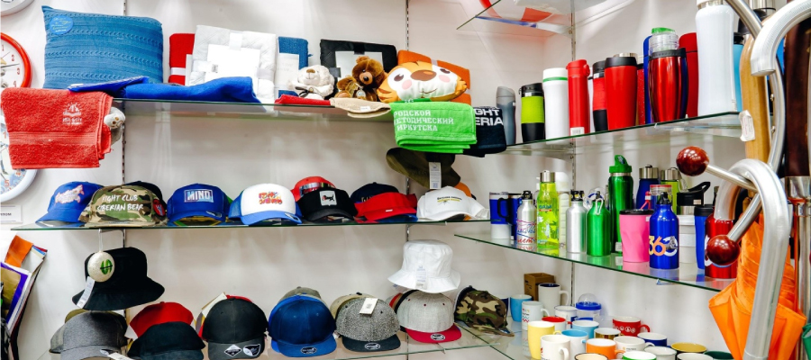 Caps, hats, mugs, and bottles are arranged in order on the promotional product shelf.