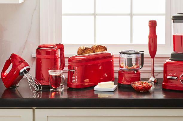 A set of kitchen products in red color, including a juicer machine, tea cup, electric kettle, and toaster, is placed on a shelf.