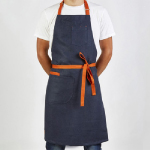 A man is standing, wearing a blue denim apron.