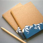 Two notebooks in khaki and blue colors are placed with a pen. They can be branded with the company's logo and used as personalized office promotional products.