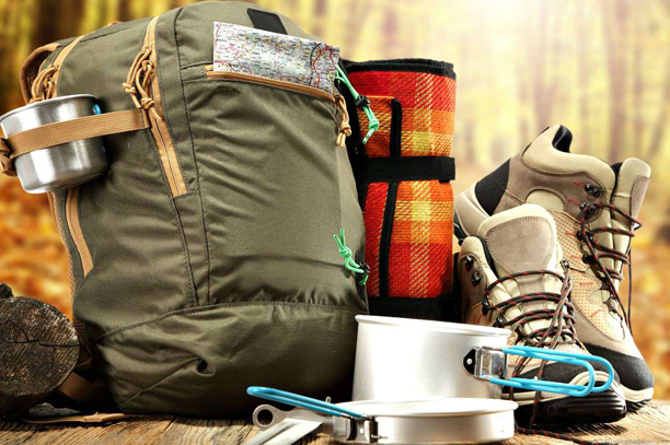 A collection of outdoor and leisure promotional products placed together, including a fully packed backpack, shoes with hook and loop fasteners, a frying pan, a pot, and a blanket.