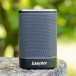 A grey Bluetooth speaker placed outdoors with a visible company logo, an excellent promotional product for outdoor and leisure activities.