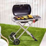 A portable grill with food frying on it, accompanied by a nearby chair.