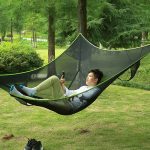 A boy using a mobile phone while lying in a portable hammock.