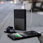 A black phone is connected to a portable charger, with a company's logo visible on it