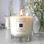 A candle is burning inside a glass jar, with an artificial flower placed in another glass jar beside it.