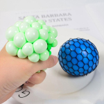A man is holding a green color stress reliever in his hand, while a blue color stress reliever is placed in front of him.