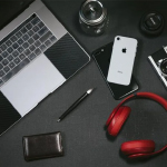 A laptop, mobile phone, smart pen, and headset are placed on a table. These items can be used as personalized promotional office products.