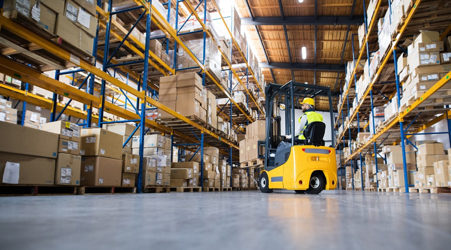 Worker driving a forklift in a warehouse with shelves full of boxes-Choosing The Right Warehouse