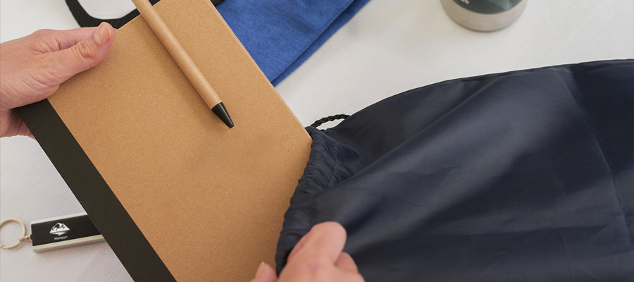 A person packing a backpack, placing an eco-friendly, customized book and pen inside.